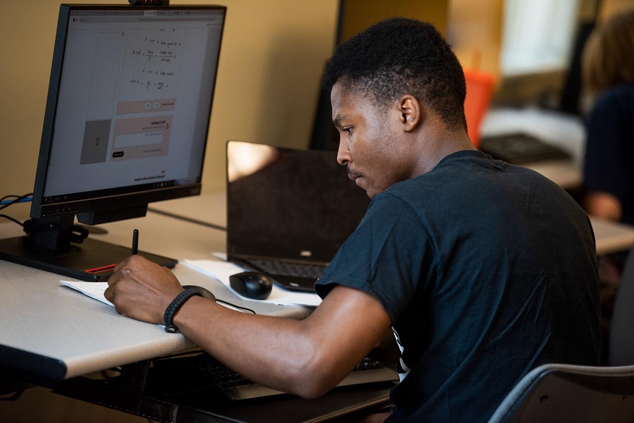 A man wearing glasses talking on the phone while sitting in front of a computer.